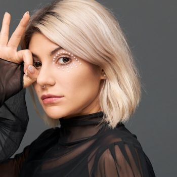 misteriosa-mujer-caucasica-joven-hermosa-maquillaje-artistico-brillante-anillo-nariz-blusa-transparente-moda-mirada-enigmatica-haciendo-gesto-dedos-su-ojo_343059-4349